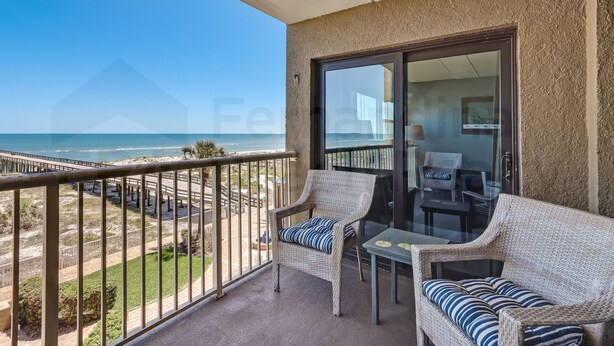 A balcony with wicker furniture, a glass door, and a view of the beach. - Upper unit Overlooking the Beautiful Outdoor Space and Pier by RedAwning (Fernandina Beach)