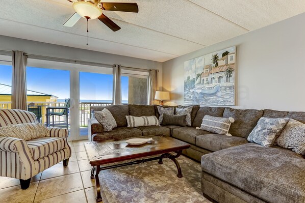 Relax in this well-appointed living room with a large sofa, armchair, and ceiling fan, offering a comfortable space to unwind.