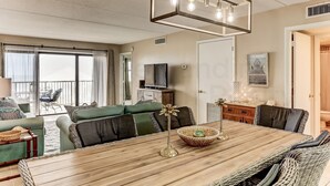 A spacious living area with a wooden dining table, green sofas, and a large window. - Comfy Upper Unit Condo to Enjoy the Beach or the Fishing by RedAwning (Fernandina Beach)