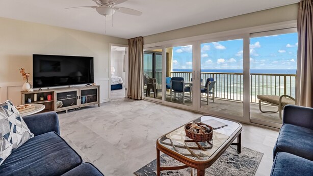 A spacious living room with a flat-screen TV, comfortable seating, a ceiling fan, and a balcony with a view of the ocean. - Oceanfront Condo with Beach Access, Pool, and Tennis Court by RedAwning (Fernandina Beach)