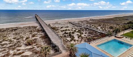 Un resort frente a la playa con un muelle largo, piscina y paseo marítimo.