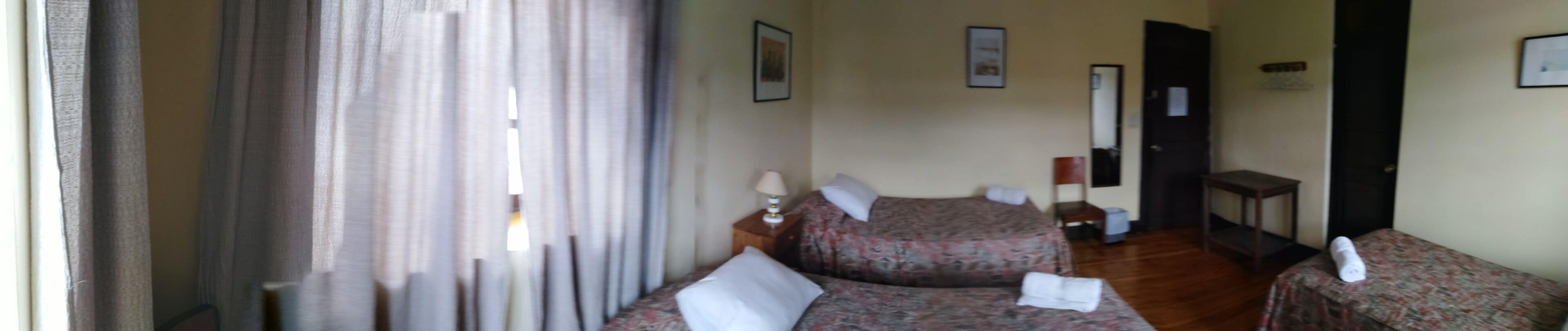 A hotel room with two beds, a bedside table with a lamp, a chair, and a small table.