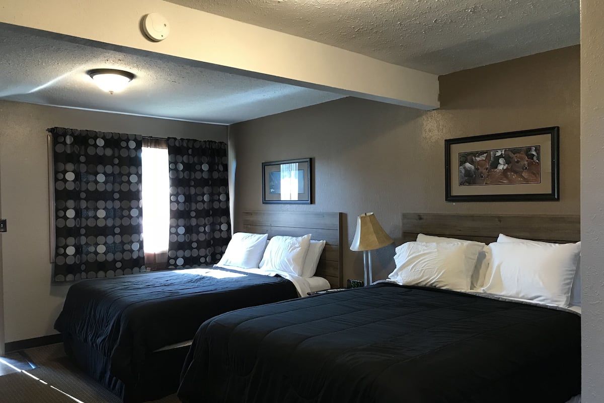 Habitación de hotel con dos camas, una ventana con cortinas de lunares, un reloj y un cuadro en la pared.