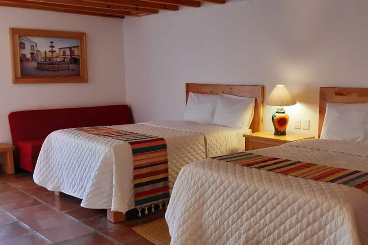 Une chambre d’hôtel avec deux lits, une chaise rouge, une table de chevet avec une lampe et un tableau au mur.