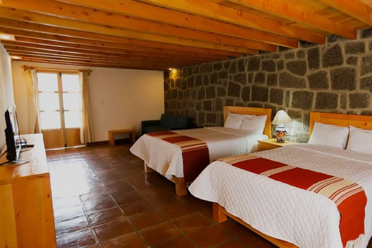 Une chambre avec deux lits, des murs en pierre, des poutres en bois, une cheminée en pierre et une fenêtre avec des rideaux.