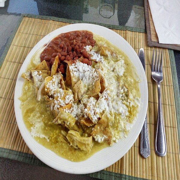 Un plato de enchiladas con frijoles y queso sobre una mesa con un tapete de bambú.