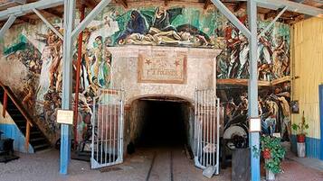 A historical building with a large mural, a staircase, and metal gates leading to an entrance.