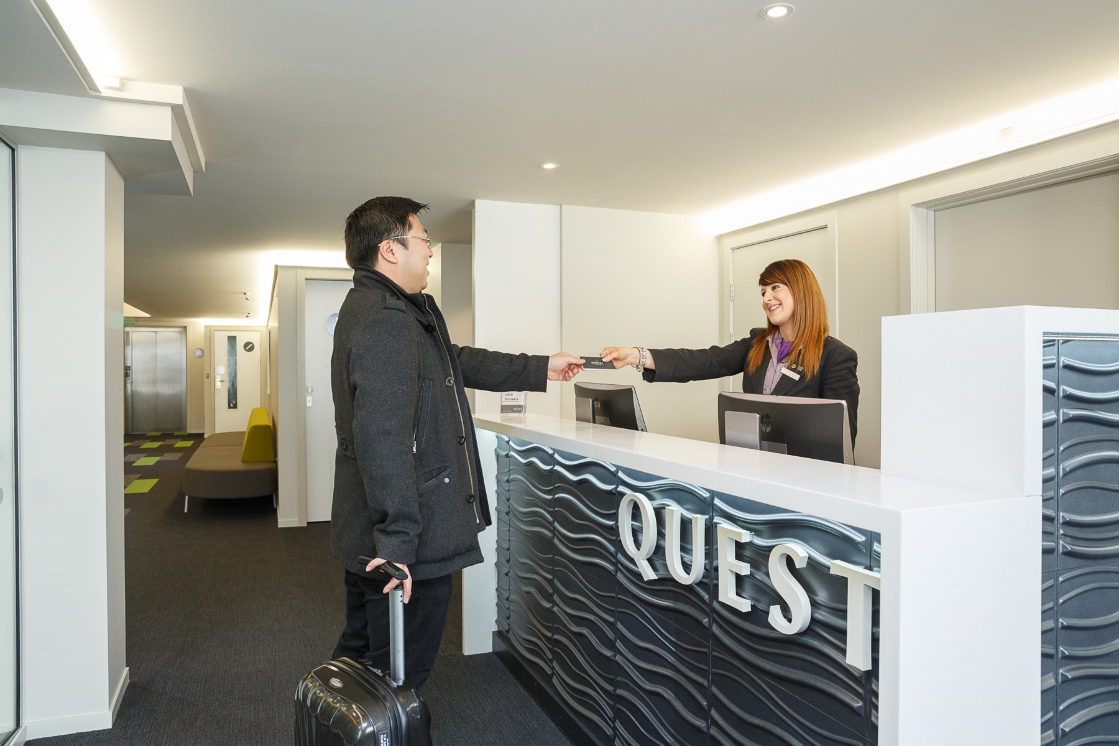 Zona de recepción de hotel con diseño moderno, un mostrador de recepción y un área de espera con sofá y sillones.