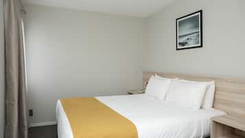 Habitación de hotel con cama, mesita de noche, teléfono, un cuadro en la pared y cortina.