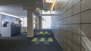 A modern hotel lobby with a reception desk, a staircase, and a tiled wall.