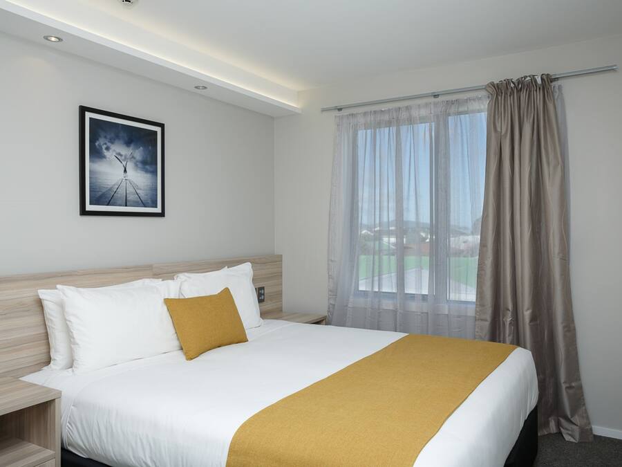 A hotel room with a large bed, a nightstand, a framed picture on the wall, and a window with curtains.
