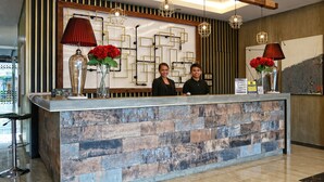 Un mostrador de recepción de diseño moderno, con fachada de madera y piedra, dos lámparas rojas y una pared decorativa con patrones geométricos.