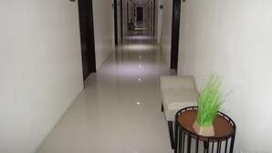 Un pasillo de hotel con un largo corredor, puertas numeradas y una pequeña mesa redonda con una planta.