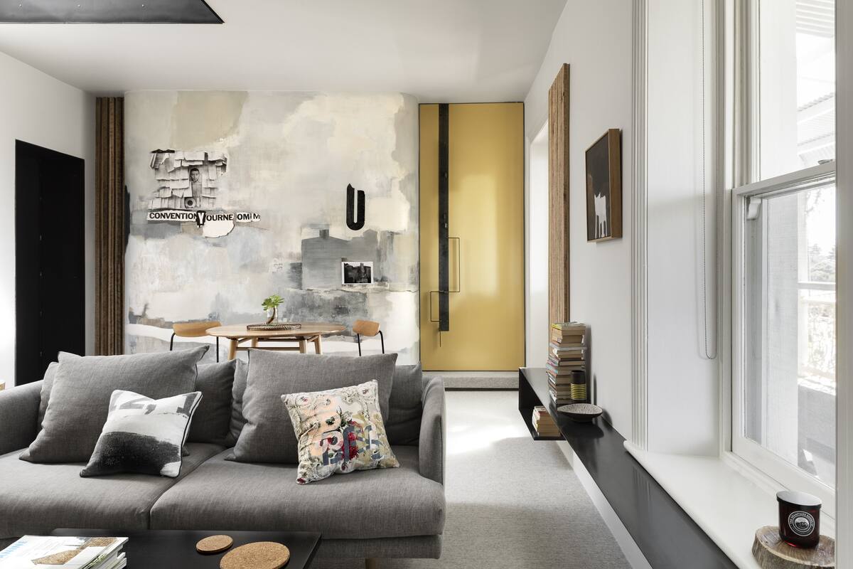 A modern living room with a grey sofa, a coffee table, and a bookshelf. There is a window with a view of the outside.
