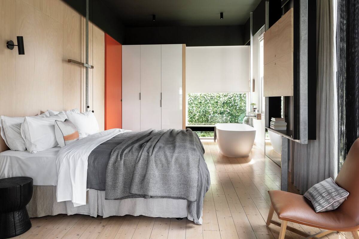 A modern bedroom with a large bed, a seating area, and a view of greenery outside.