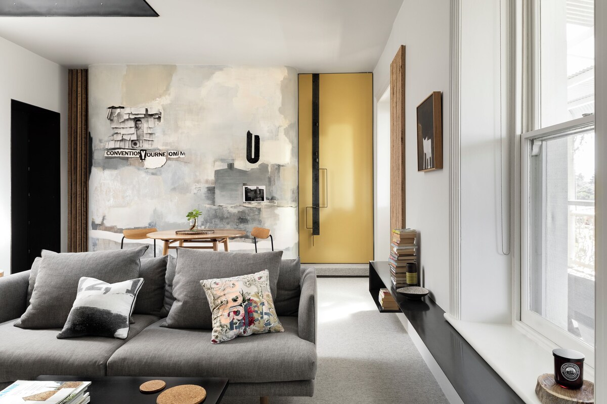 Una sala de estar moderna con un sofá gris, una mesa de centro y una estantería. Se ve una ventana con vistas al exterior.