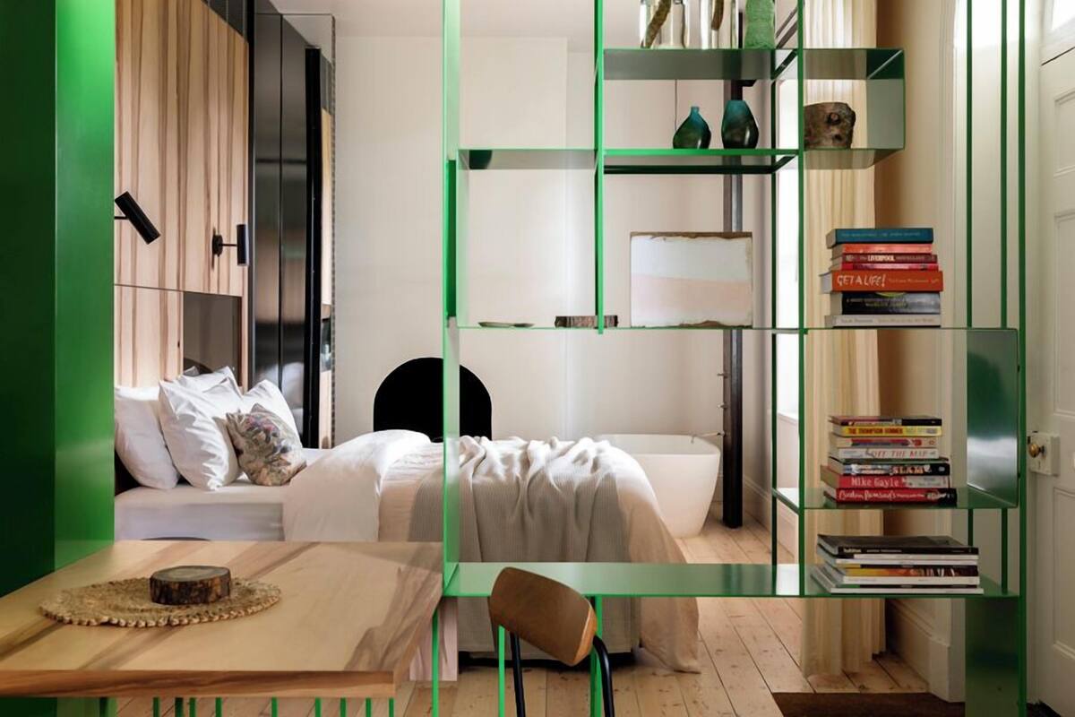 A modern bedroom with a bed, bedside tables, a bookshelf, and a mirror.