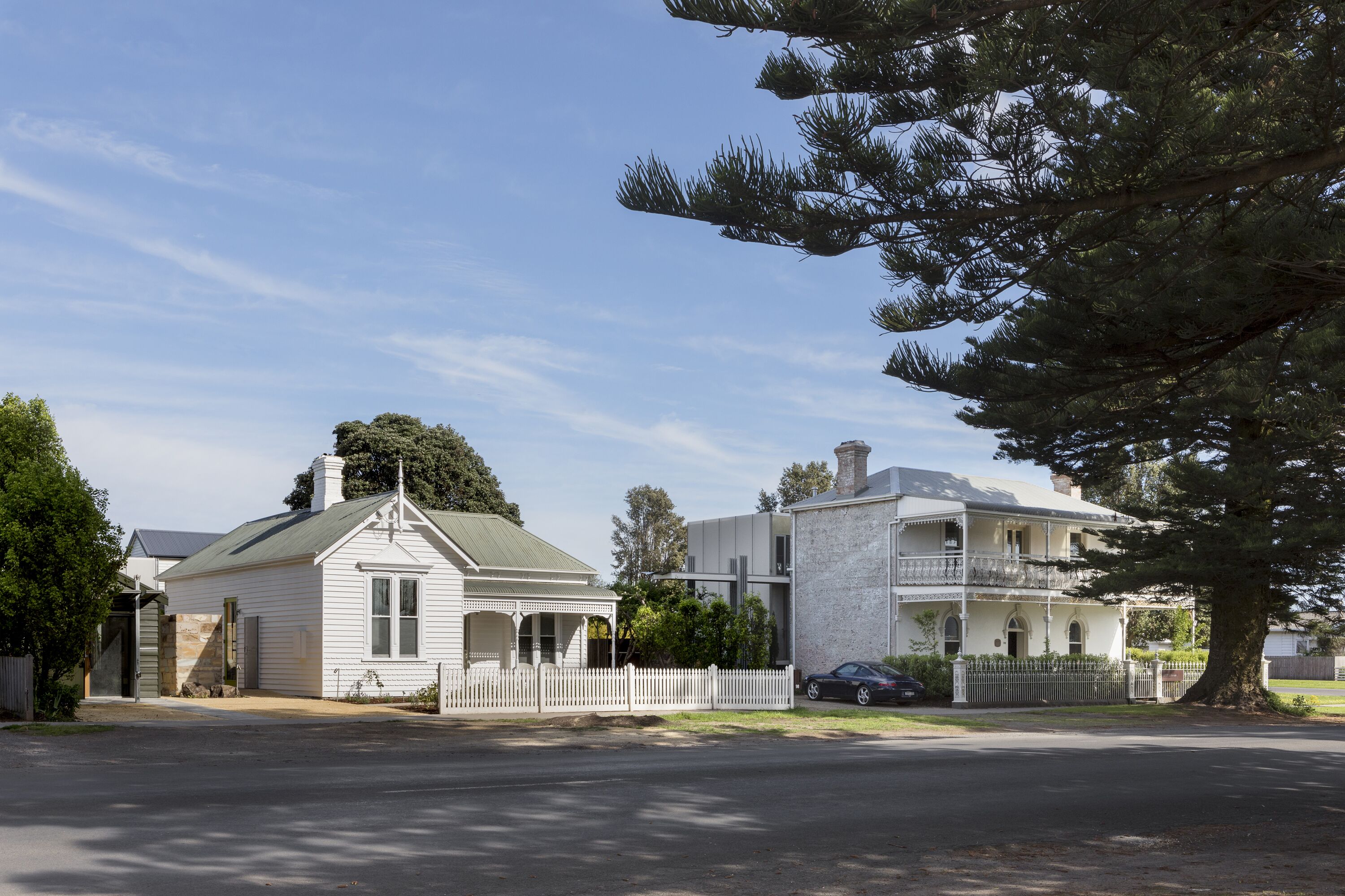 A two-story house with a white exterior, a green roof, and a white picket fence.