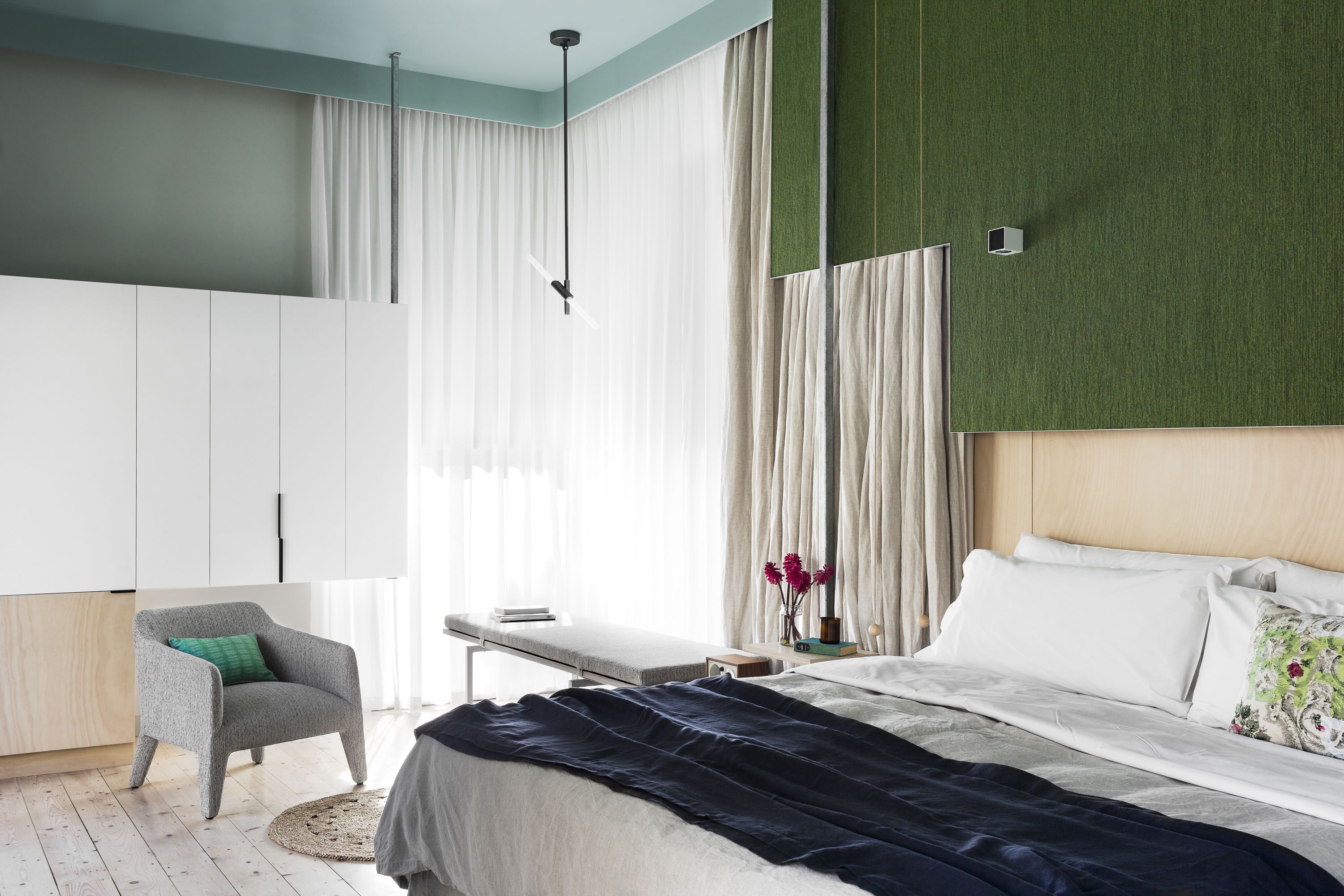 Un dormitorio moderno con cama, sillón, mesita de noche y armario.