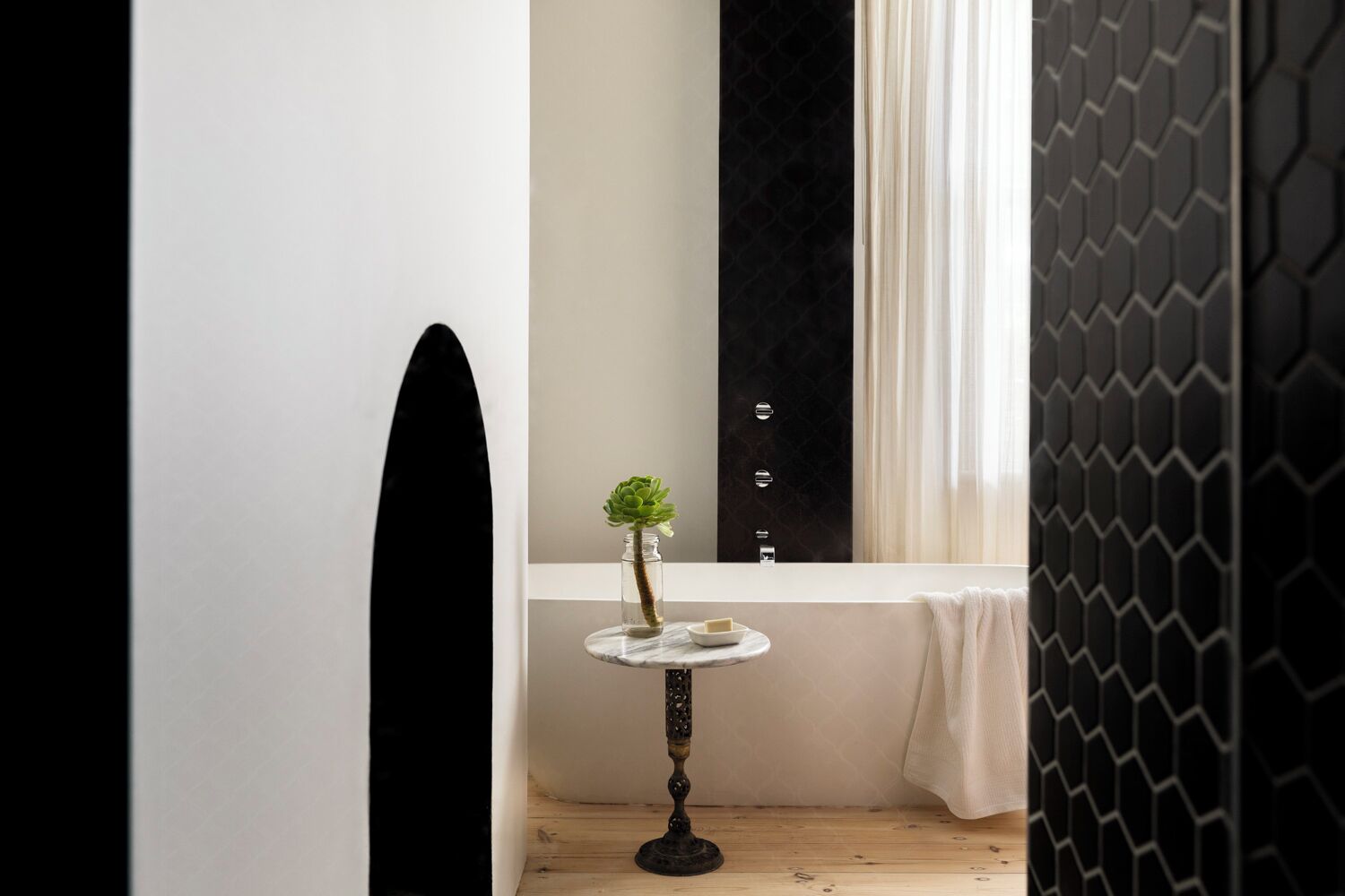 A bathroom with a black and white tiled wall, a small round table with a vase of green plants, and a white towel hanging on the wall.