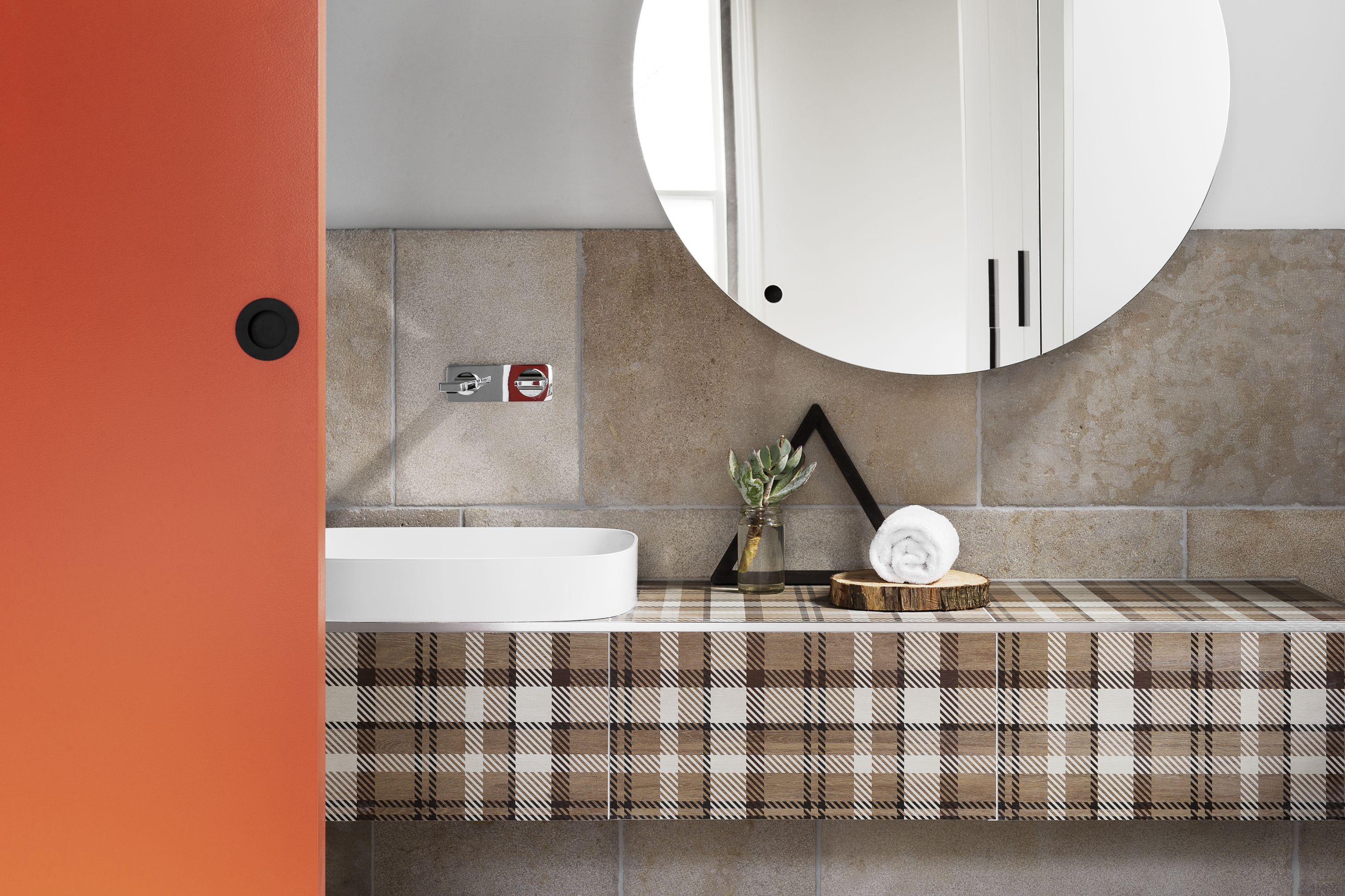 A modern bathroom with a white bathtub, a round mirror, and a checkered tile backsplash.