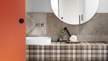 A modern bathroom with a white bathtub, a round mirror, and a checkered tile backsplash.