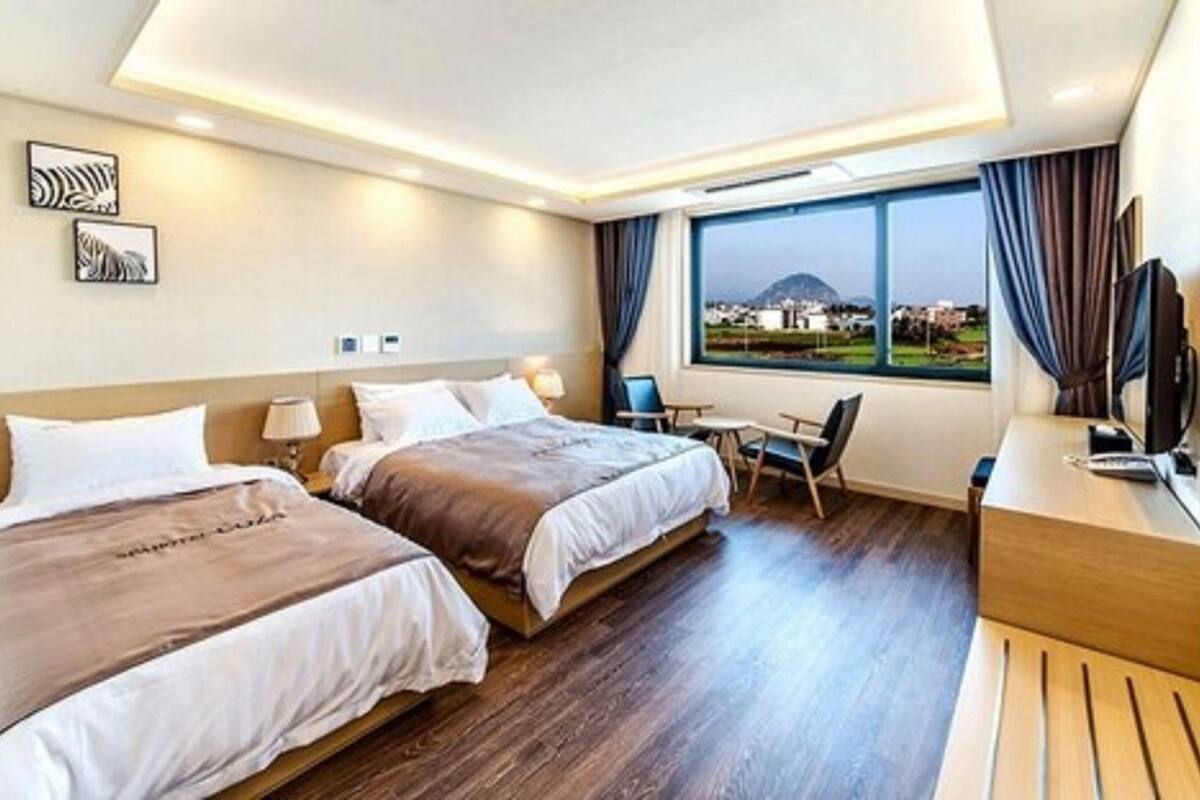Hotelkamer met twee bedden, een bureau, een stoel, een televisie en een groot raam met uitzicht.