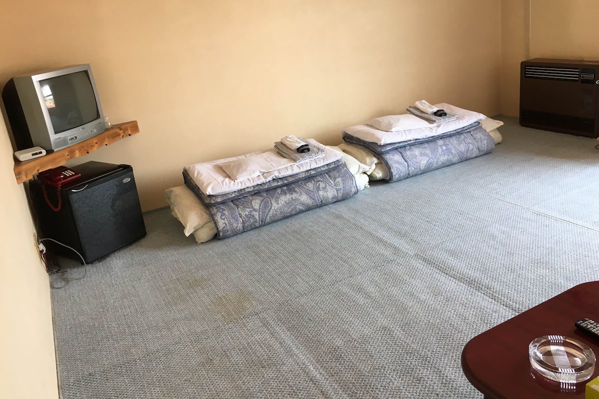 A compact room with two beds, a small refrigerator, a television on a shelf, and a heater.