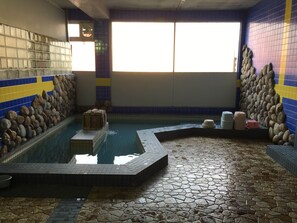 A swimming pool with a stone wall and tiled floor, surrounded by a tiled wall with blue and yellow accents. - Hokuseiso (Furano)