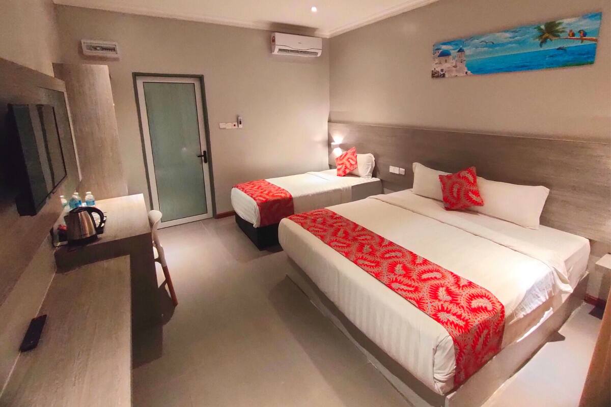 A hotel room with two beds, a small table with a kettle, a TV, and an air conditioning unit.