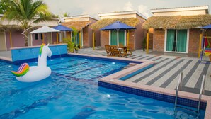A swimming pool with a swan float, thatched-roof huts, and a lounge area with chairs and a table. - Lavigo Resort (Langkawi)