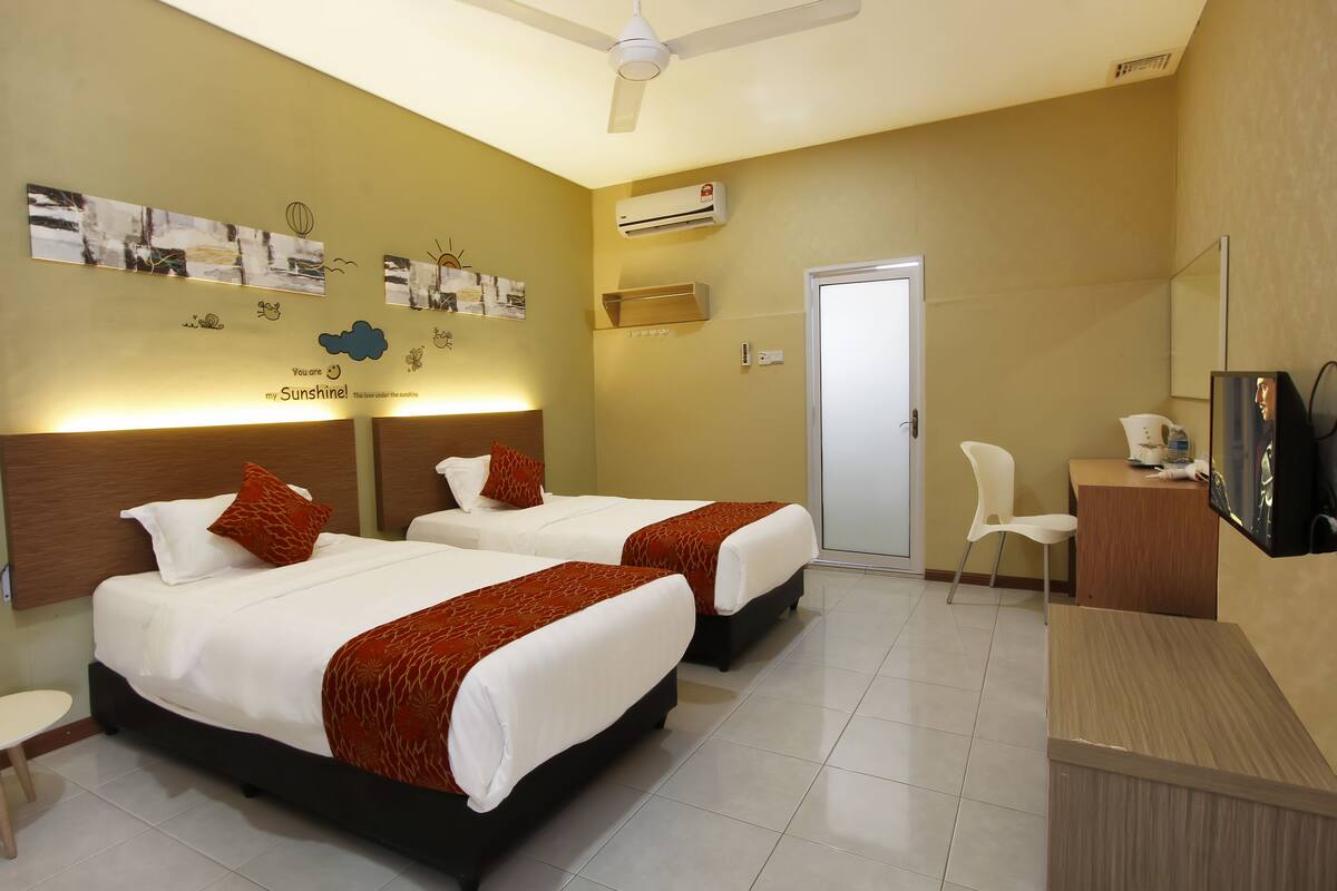 A hotel room with two beds, a desk, a chair, a TV, and artwork on the walls.