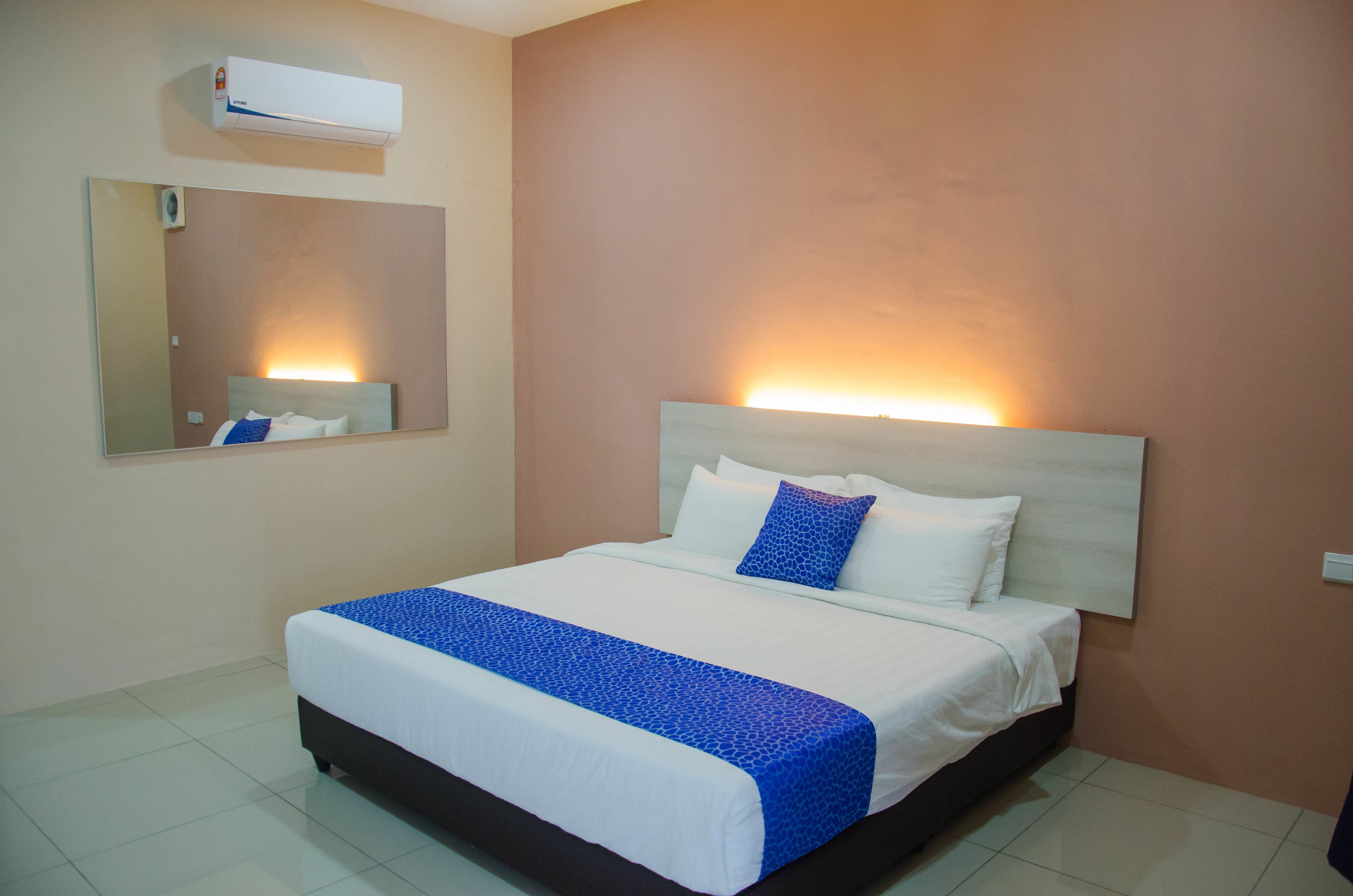 Habitación de hotel con una cama grande, cabecero con iluminación integrada, aire acondicionado de pared y un espejo sobre la cama.