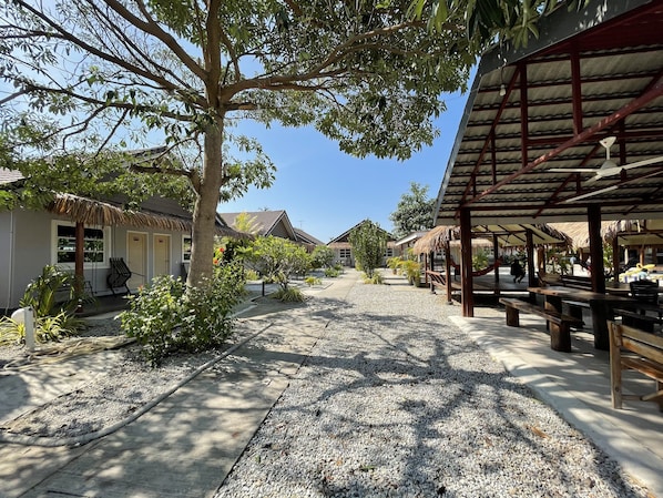 A resort area with thatched-roof buildings, outdoor seating, and a gravel pathway.