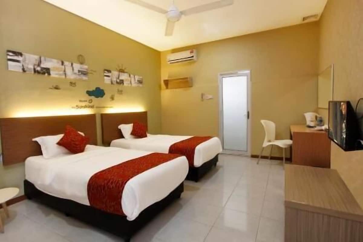 A hotel room with two beds, a desk, a chair, a TV, and a ceiling fan.