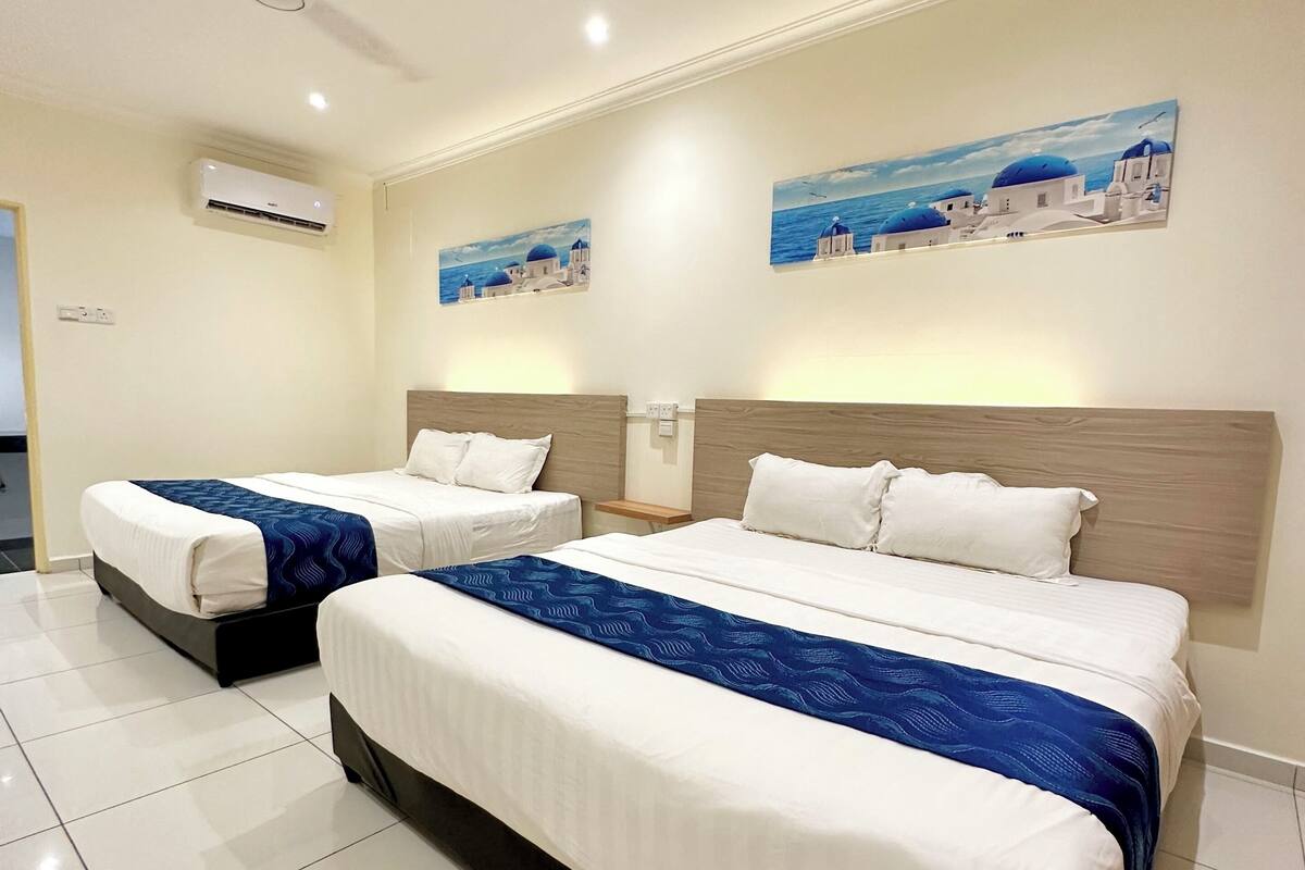 A hotel room with two beds, a ceiling fan, wall-mounted air conditioning, and two paintings of coastal scenes.