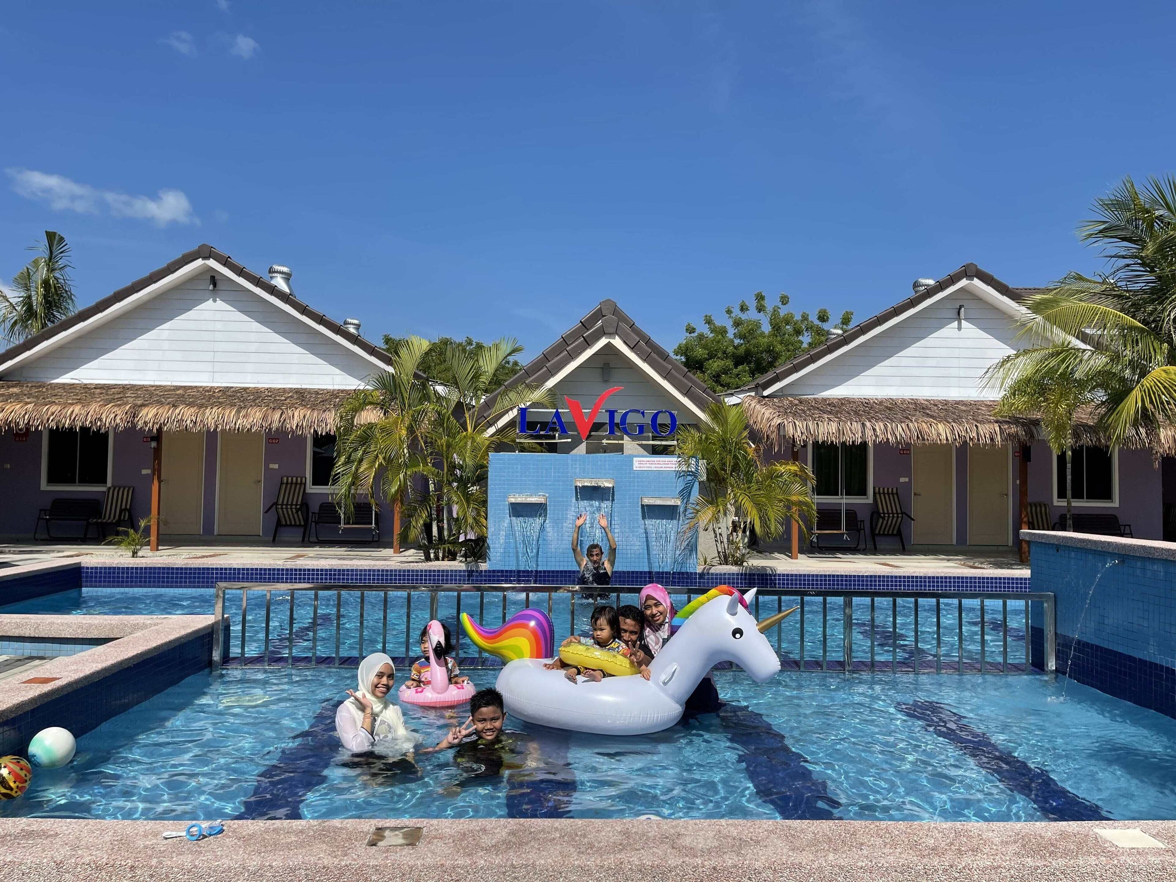 A swimming pool area with a water slide, inflatable unicorn float, and palm trees.