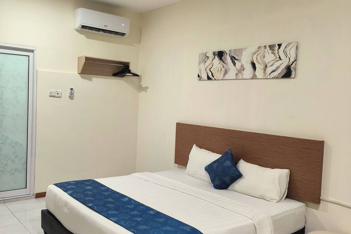A hotel room with a bed, a ceiling fan, an air conditioning unit, a wall-mounted artwork, and a small table.