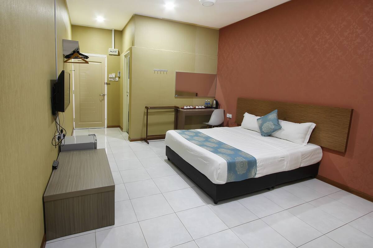 A hotel room with a bed, a desk, a chair, a TV, and a wardrobe.