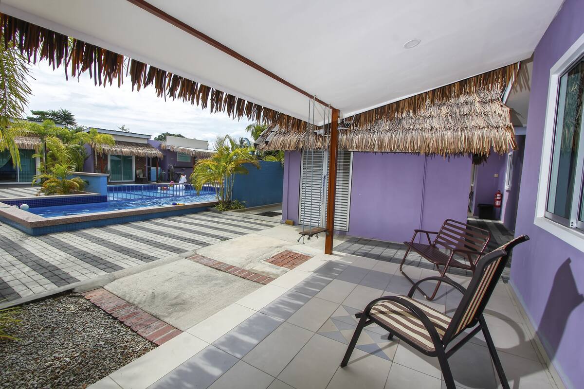A pool area with a thatched roof, a seating area with chairs, and a view of a neighboring building.