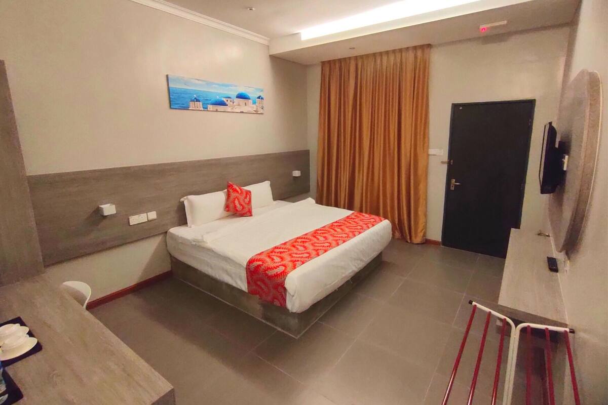 A hotel room with a bed, a desk, a chair, a TV, and a painting on the wall.