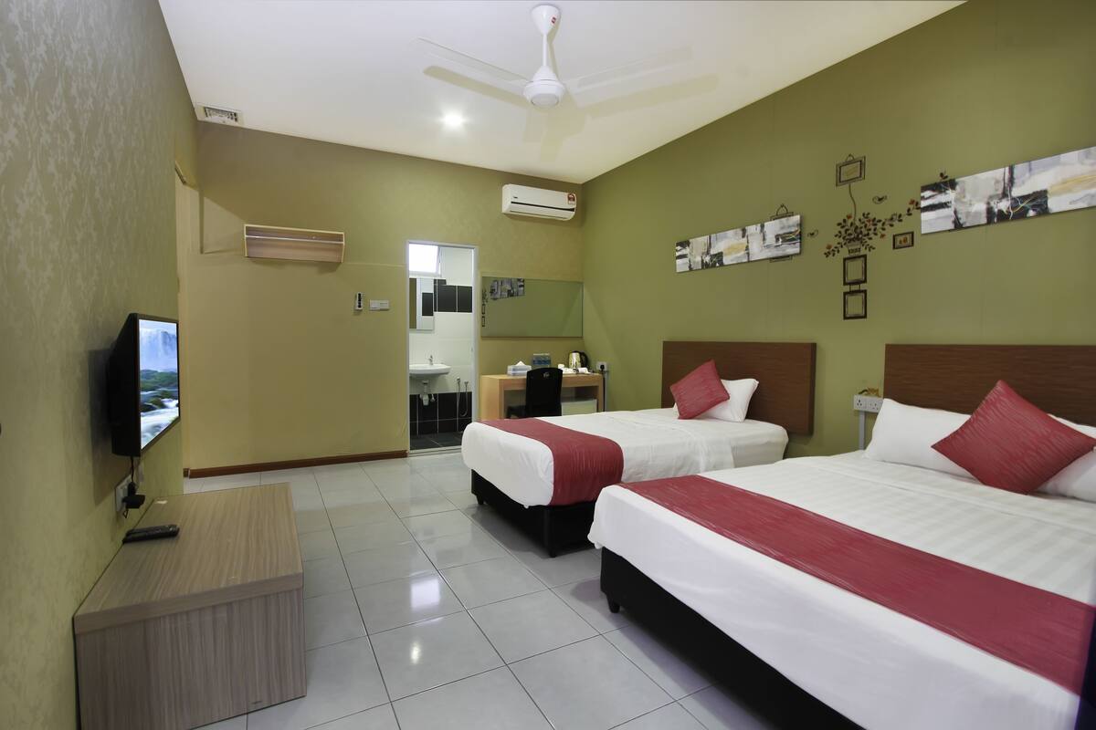 A hotel room with two beds, a TV, an air conditioner, and a desk with a chair.