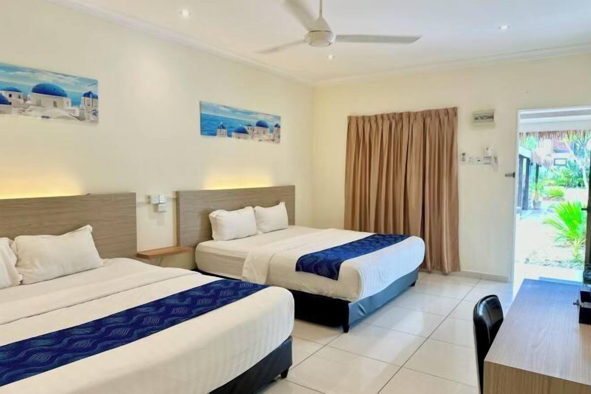 A hotel room with two beds, a desk, and a view of the outside.