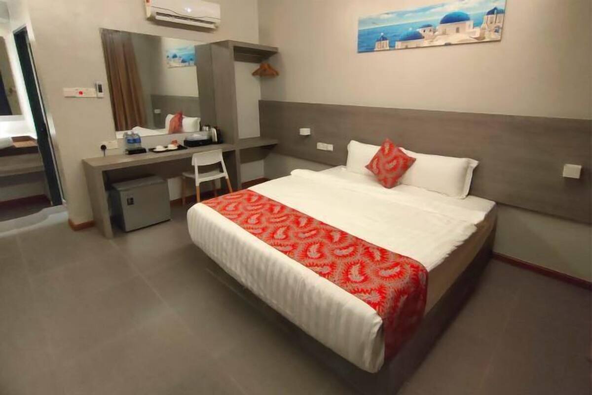 A hotel room with a bed, desk, chair, and a large mirror.