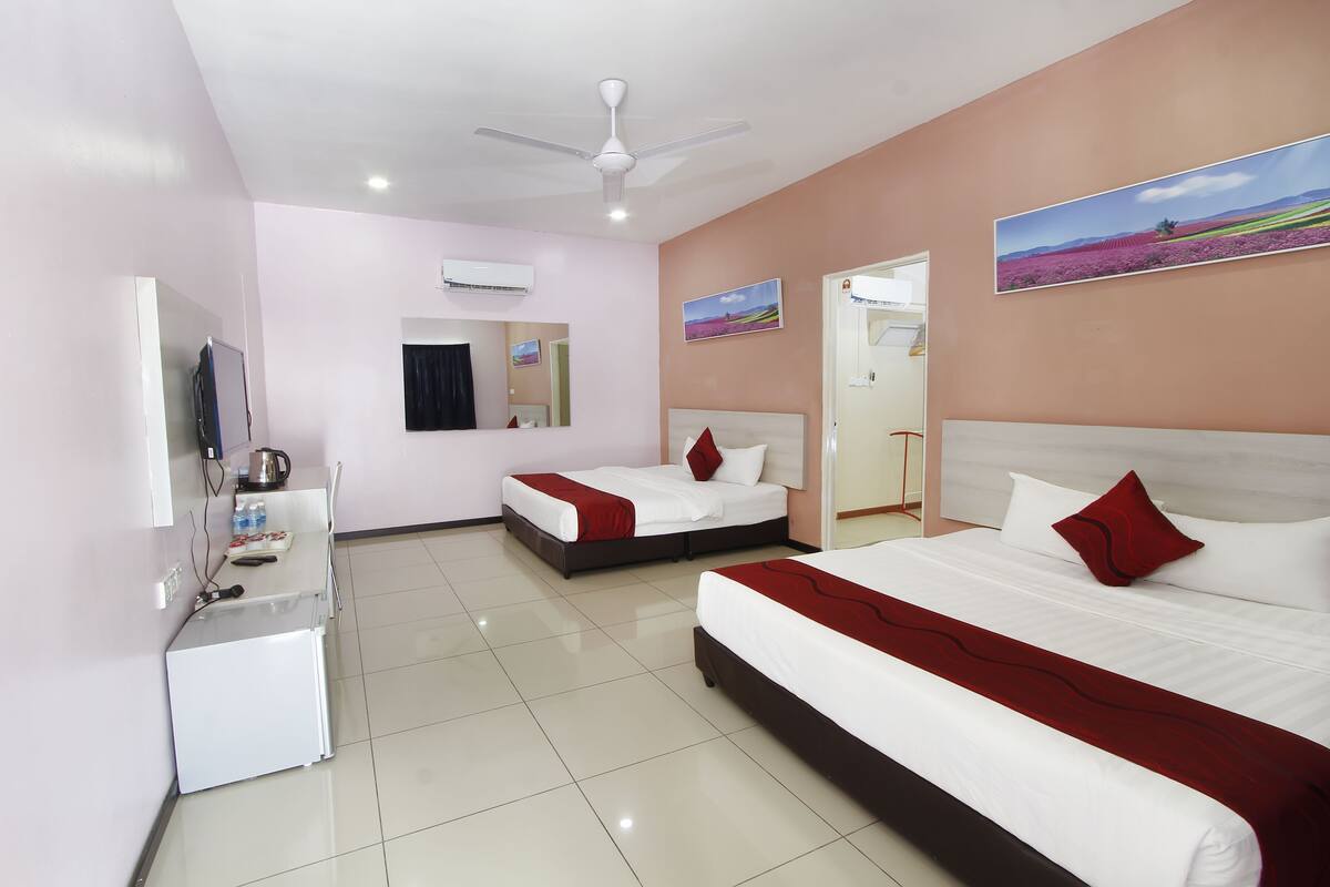 A hotel room with two beds, a small kitchenette, a ceiling fan, and a painting on the wall.
