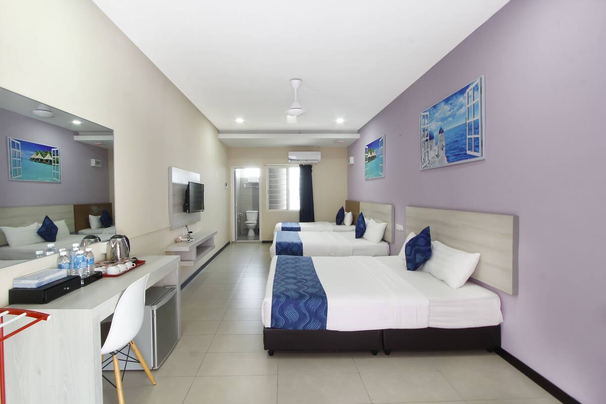 A hotel room with two beds, a desk, a TV, and a bathroom.