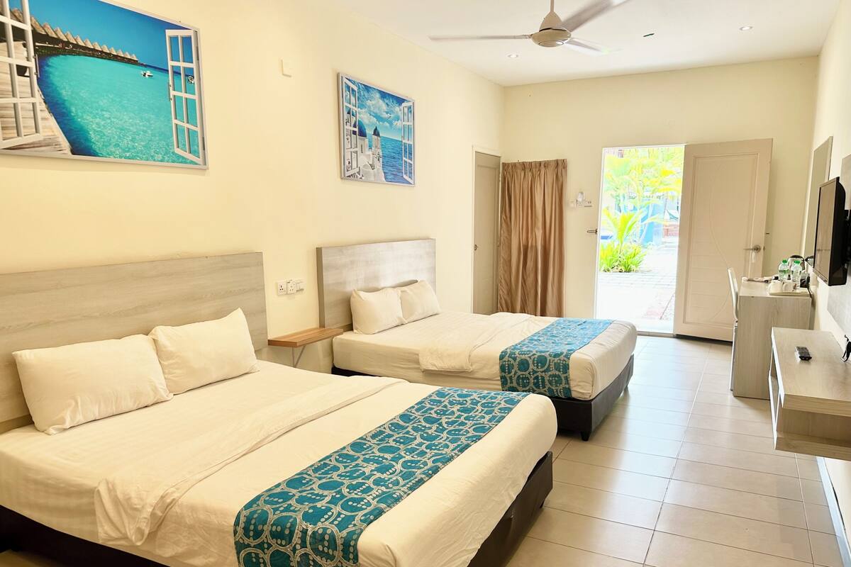 A hotel room with two beds, a desk, a TV, and a view of a pool.