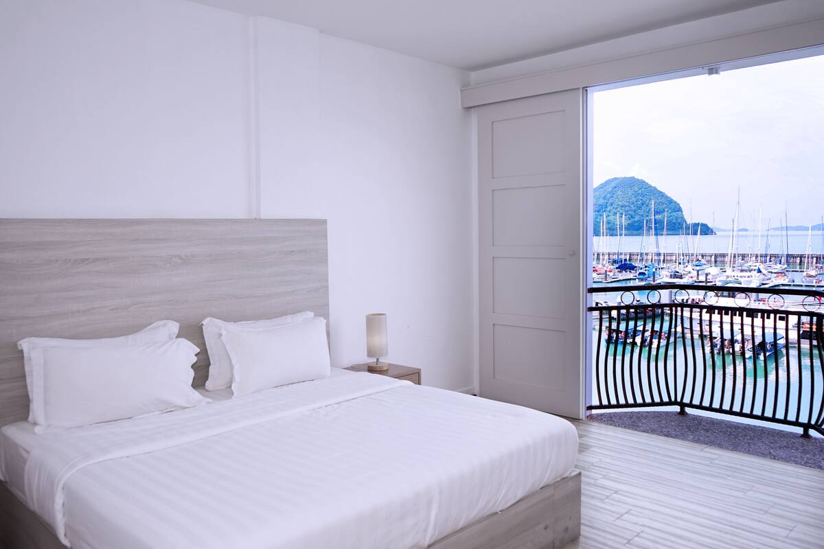 Une chambre d’hôtel avec un grand lit, une table de chevet et une vue sur un port de plaisance avec des bateaux.
