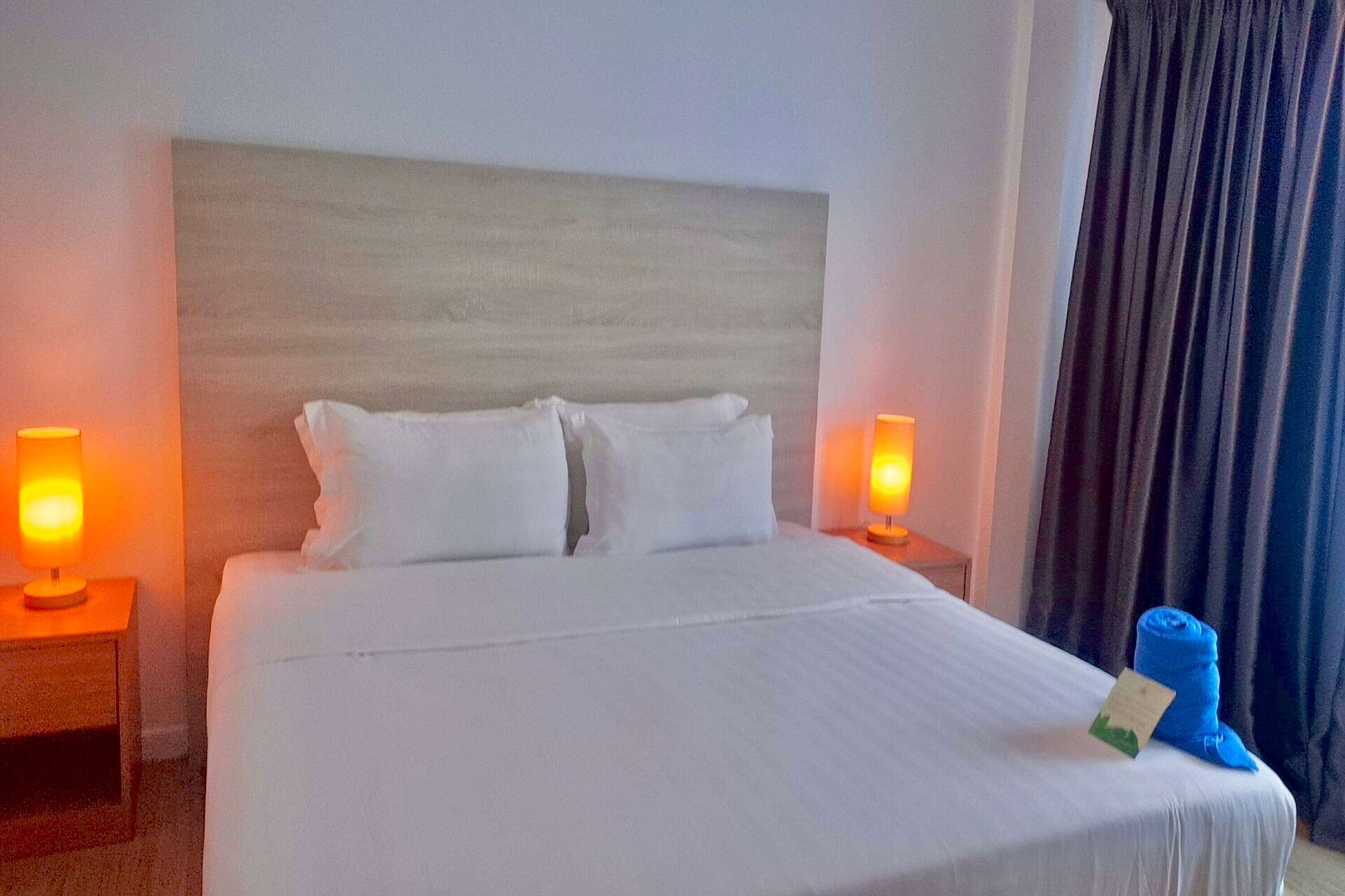 Ein Hotelzimmer mit einem großen Bett, zwei Nachttischlampen, einem Kopfteil und einem blauen Handtuch auf dem Bett.