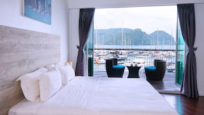 Ein Hotelzimmer mit einem großen Bett, Blick auf einen Yachthafen und einem Balkon mit Stühlen.